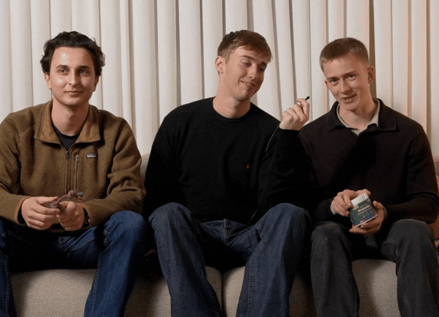 Tre unge mænd på sofa, én holder en krukke med probiotika, de smiler og viser produktet