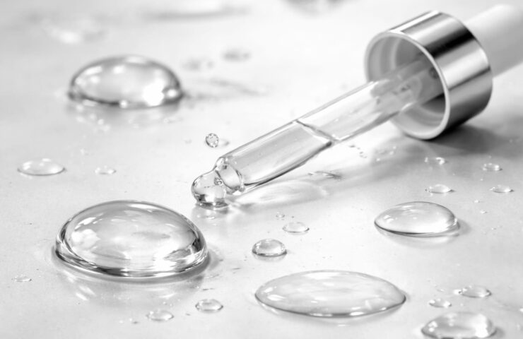 Pipette med hyaluronsyre-serum og klare dråber på lys overflade